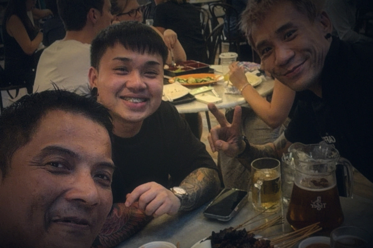 Matthew Poh with two TCE teammates around a hawker centre table in Singapore, laughing together over a shared meal
