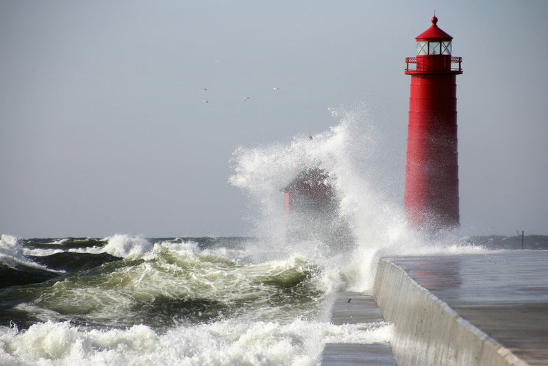 Waves crashing against a red lighthouse under a grey sky