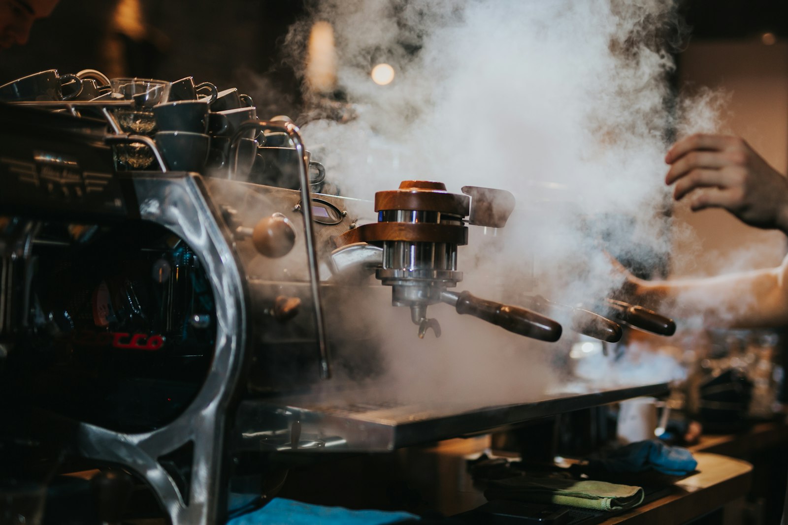 Steam rising from an espresso machine group head in a dimly lit café before service — the unseen, ordinary work of ministry
