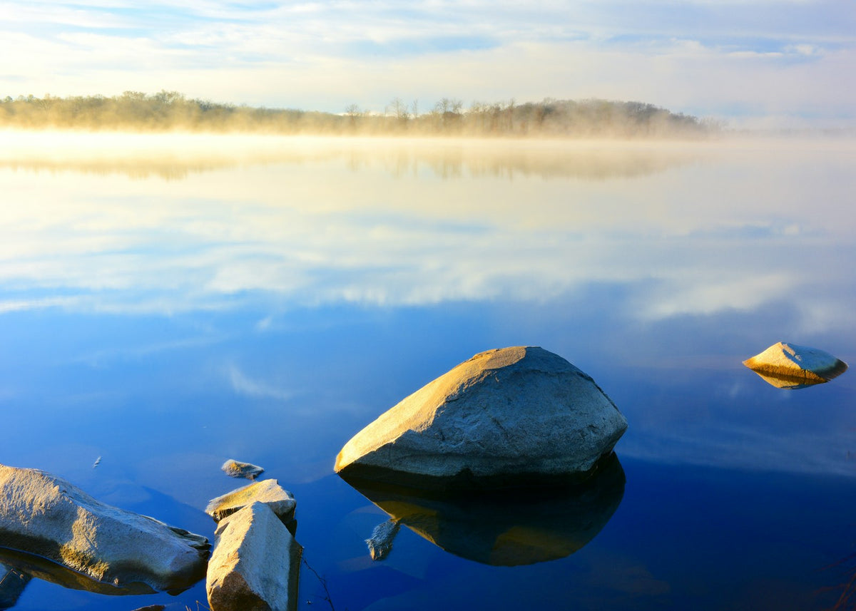 Misty morning sunrise over a calm lake with rocks