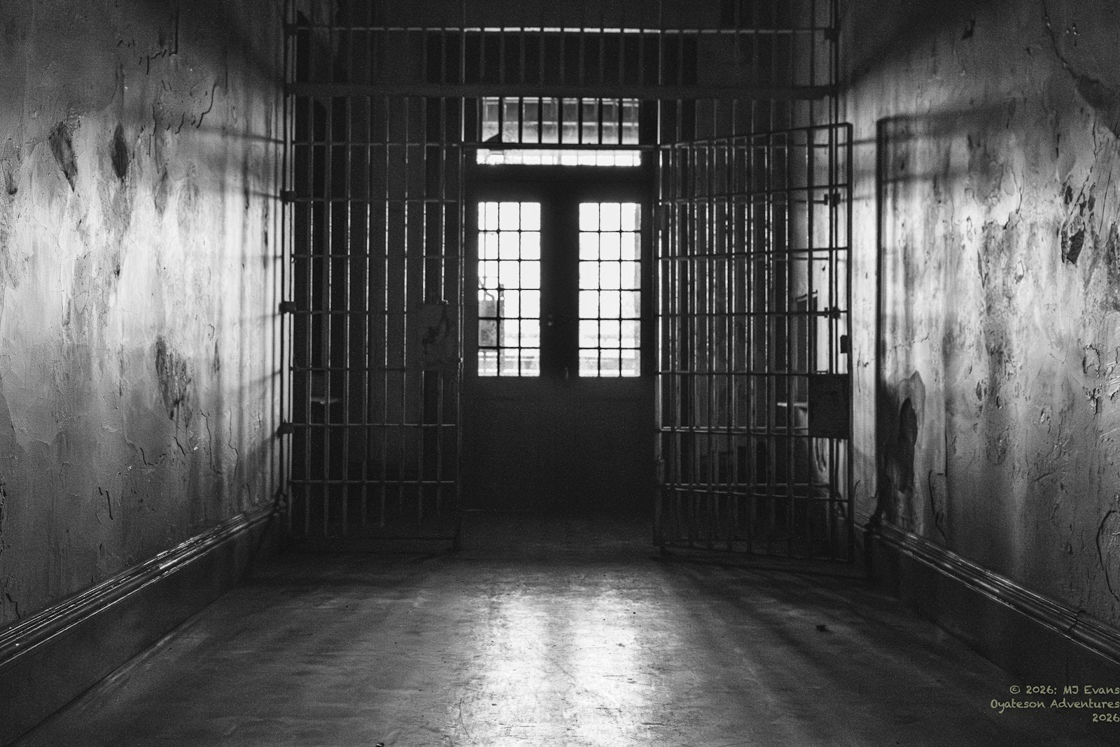 A dark, empty prison hallway with cell doors standing open