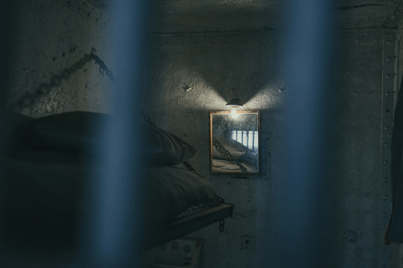 A dimly lit prison cell with a bed and a barred window