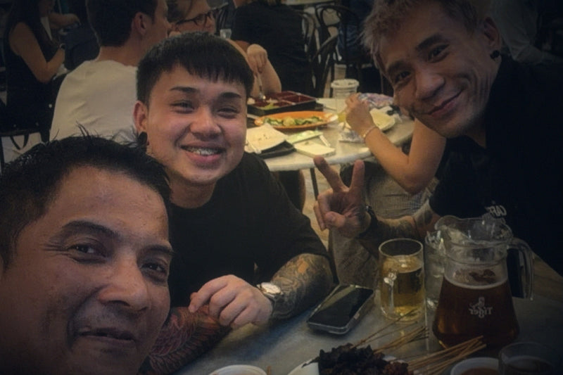Matthew Poh with two TCE teammates around a hawker centre table in Singapore, laughing together over a shared meal