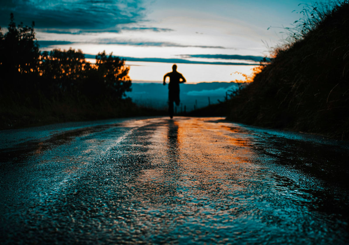 Silhouette of a person running on an open road at sunrise