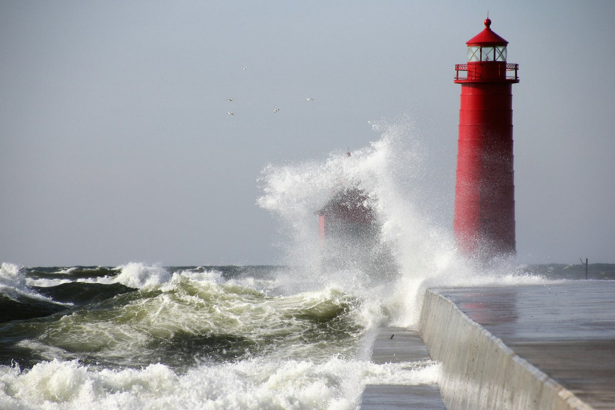 Waves crashing against a red lighthouse under a grey sky