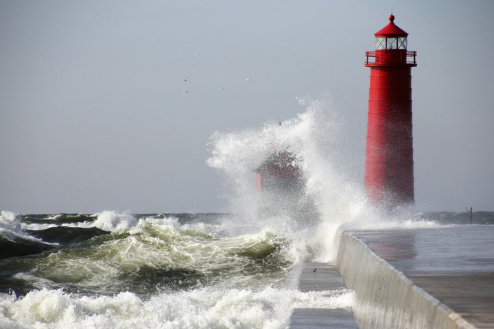 Waves crashing against a red lighthouse under a grey sky
