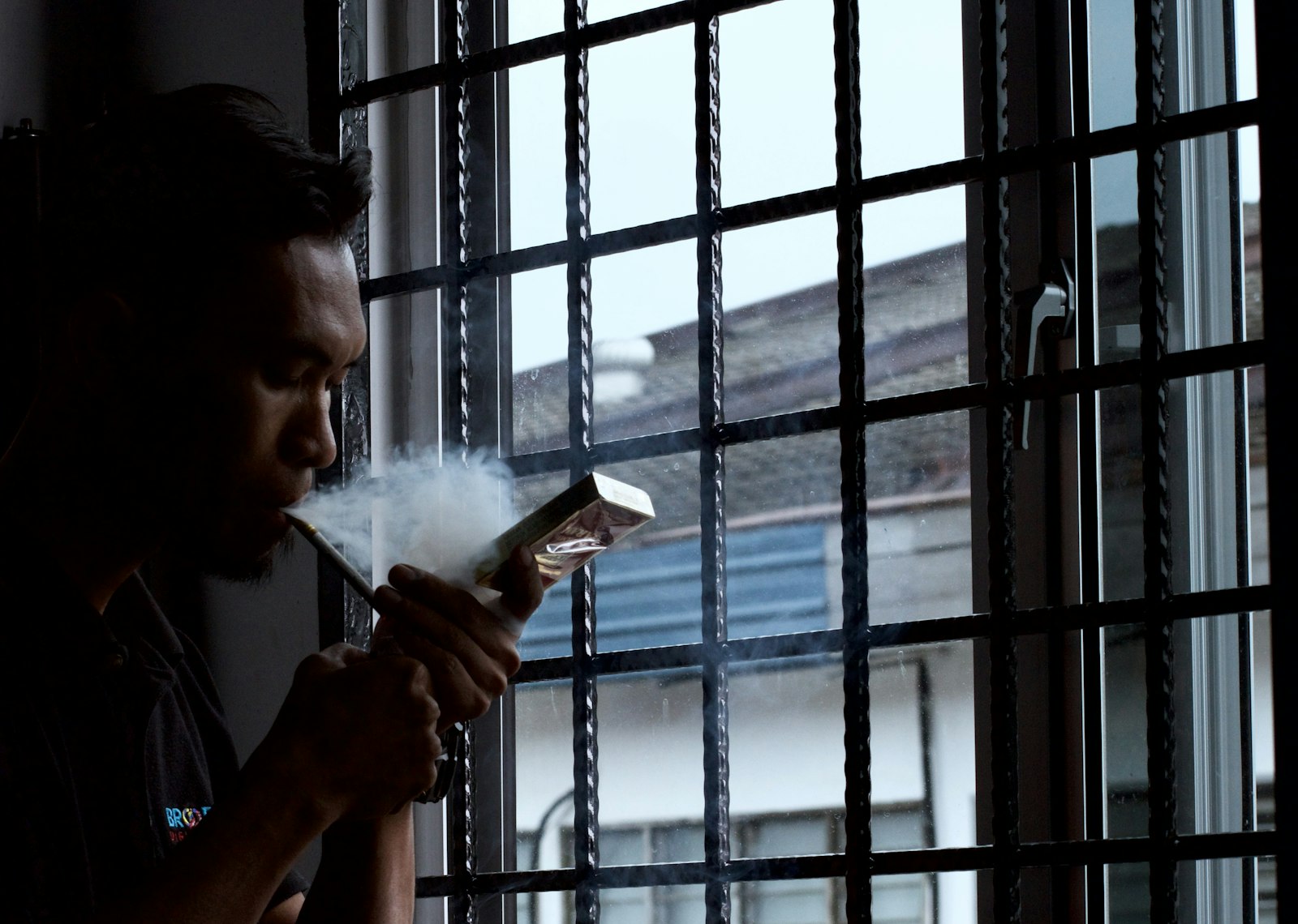 A person blowing smoke beside a dim window