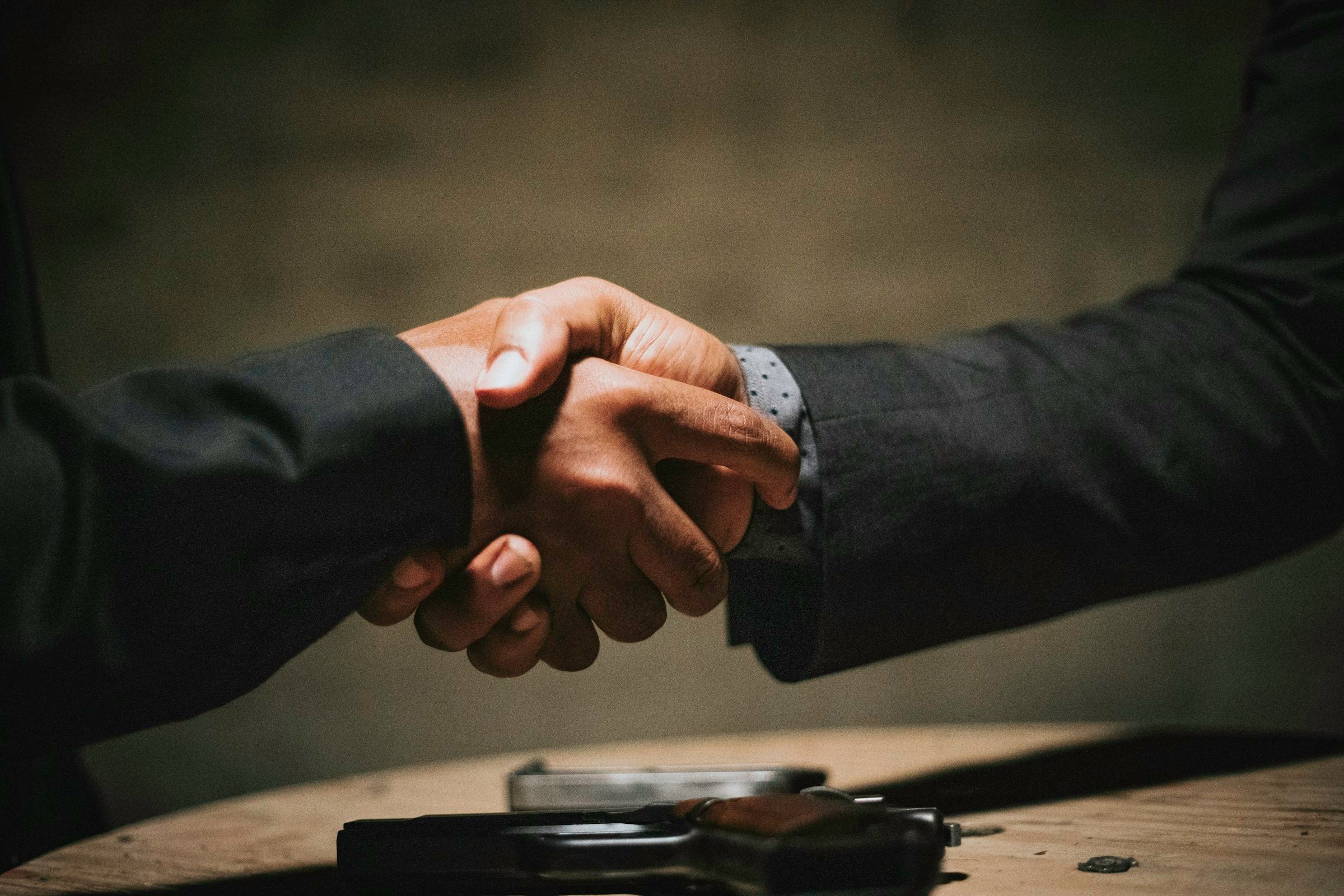 Two hands meeting over a wooden table — in the cafe trade, every cup is a small covenant. Photo by Rock Staar on Unsplash.