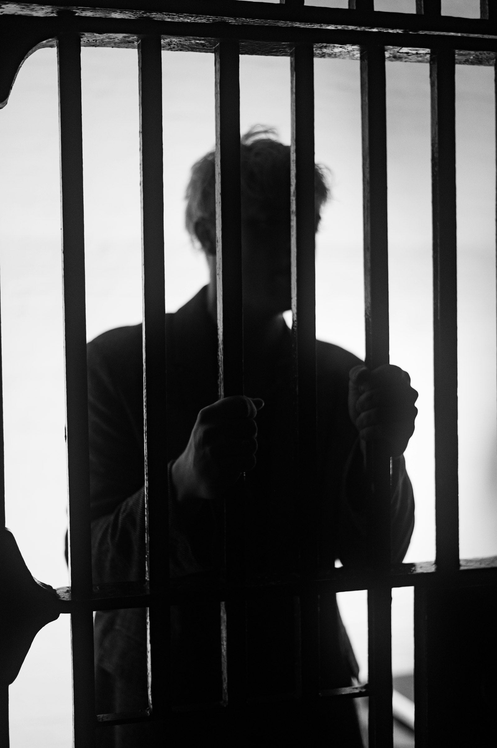 A man's silhouette gripping prison bars in black and white