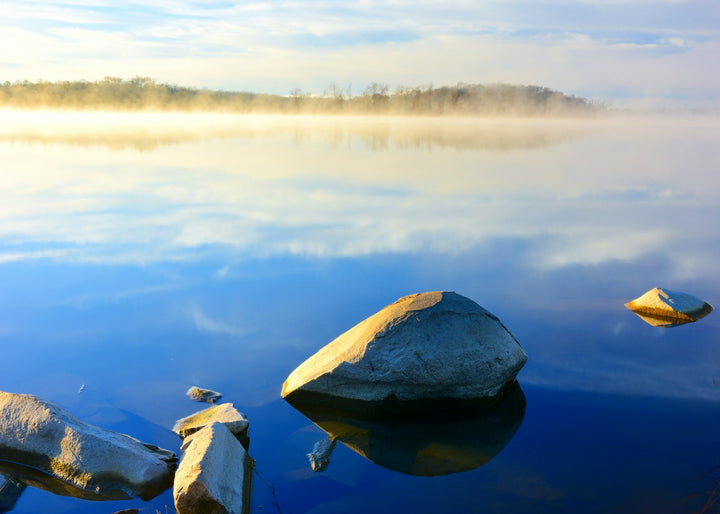 Misty morning sunrise over a calm lake with rocks