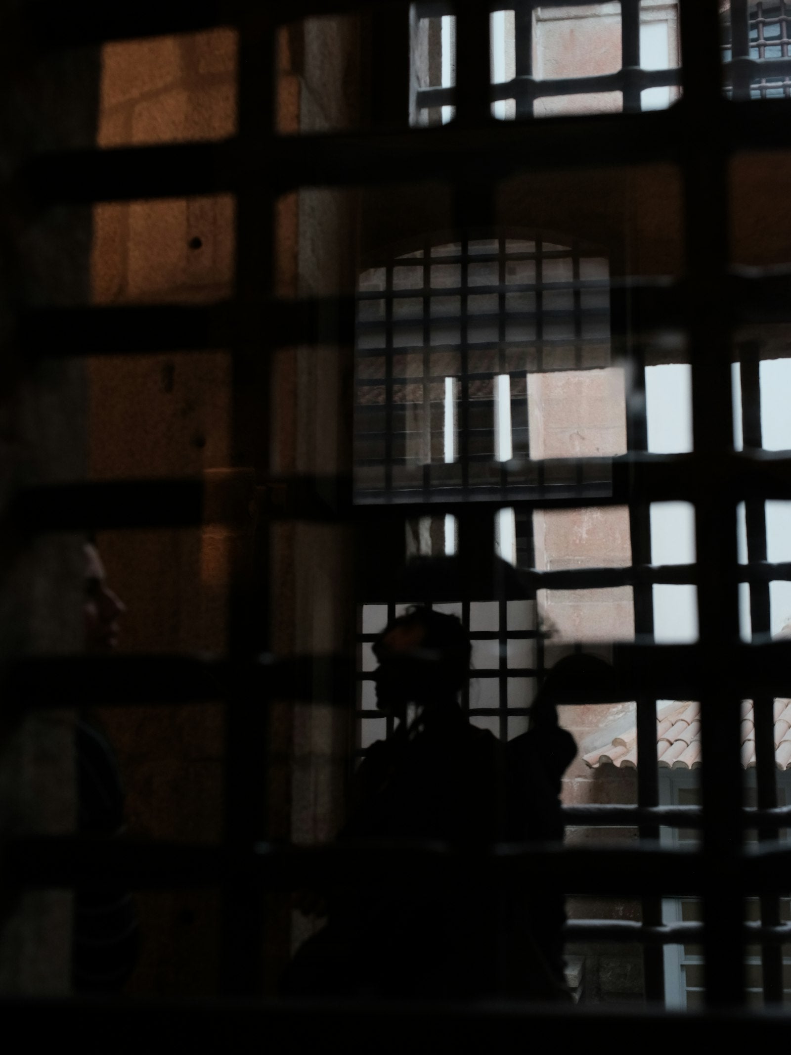 Two figures glimpsed through prison bars in dim light