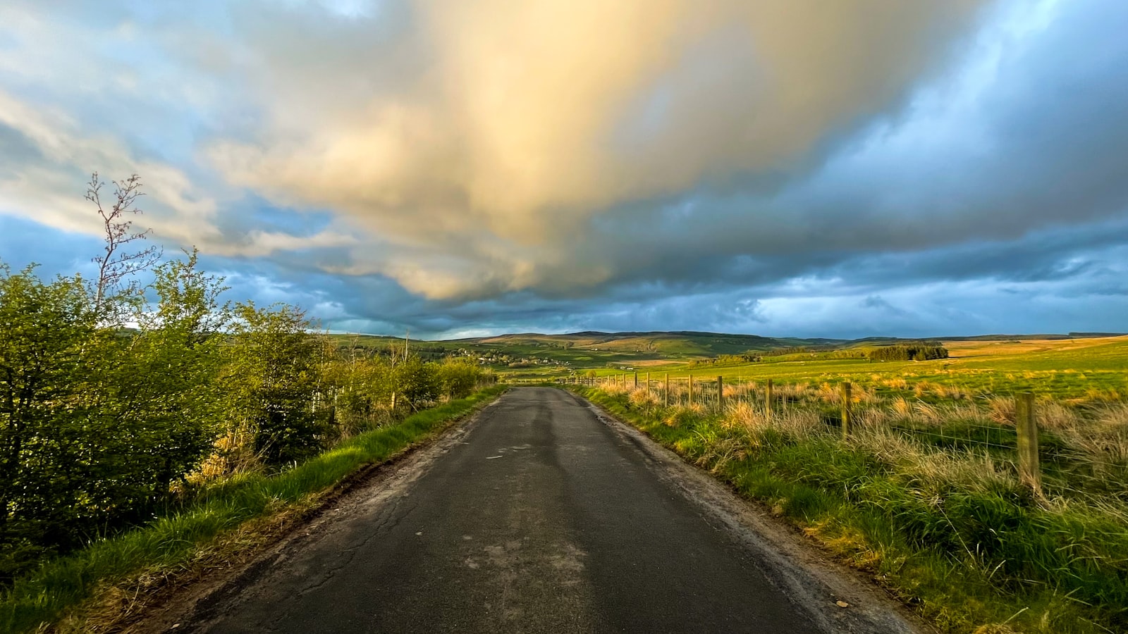 An empty road through green fields under a dramatic sky — the road of the Good Samaritan